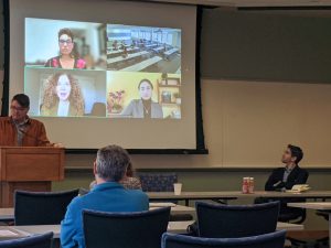 Scholars speak projected on a screen as people listen and watch them speak. 