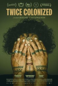 A woman with free curly hair covers her eyes with her tatooed hands. 
