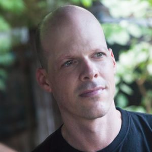 Headshot of a man looking off into the distance and wearing a black t-shirt. 